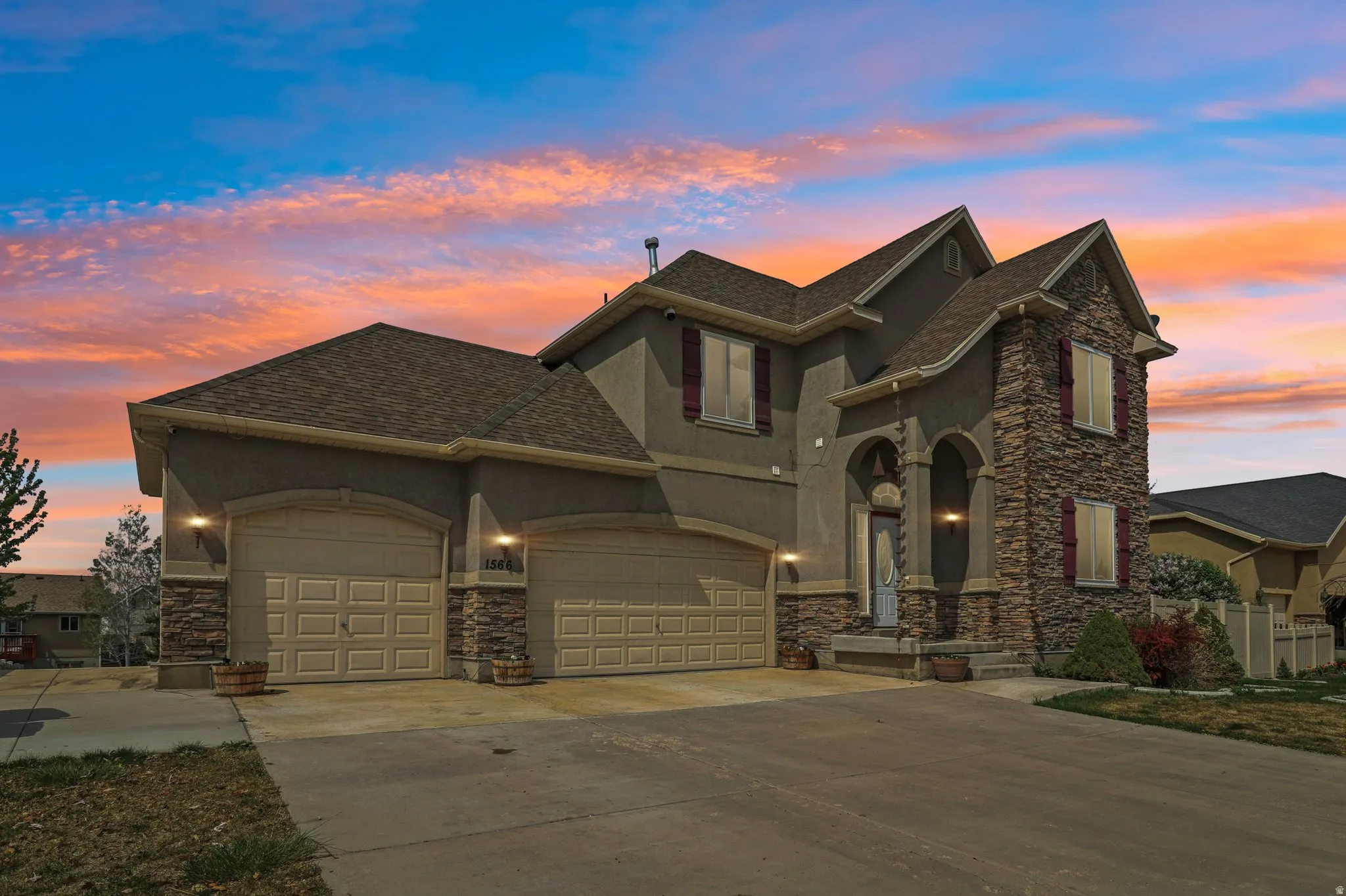 View of front of house featuring stone siding, stucco siding, roof with shingles, and driveway