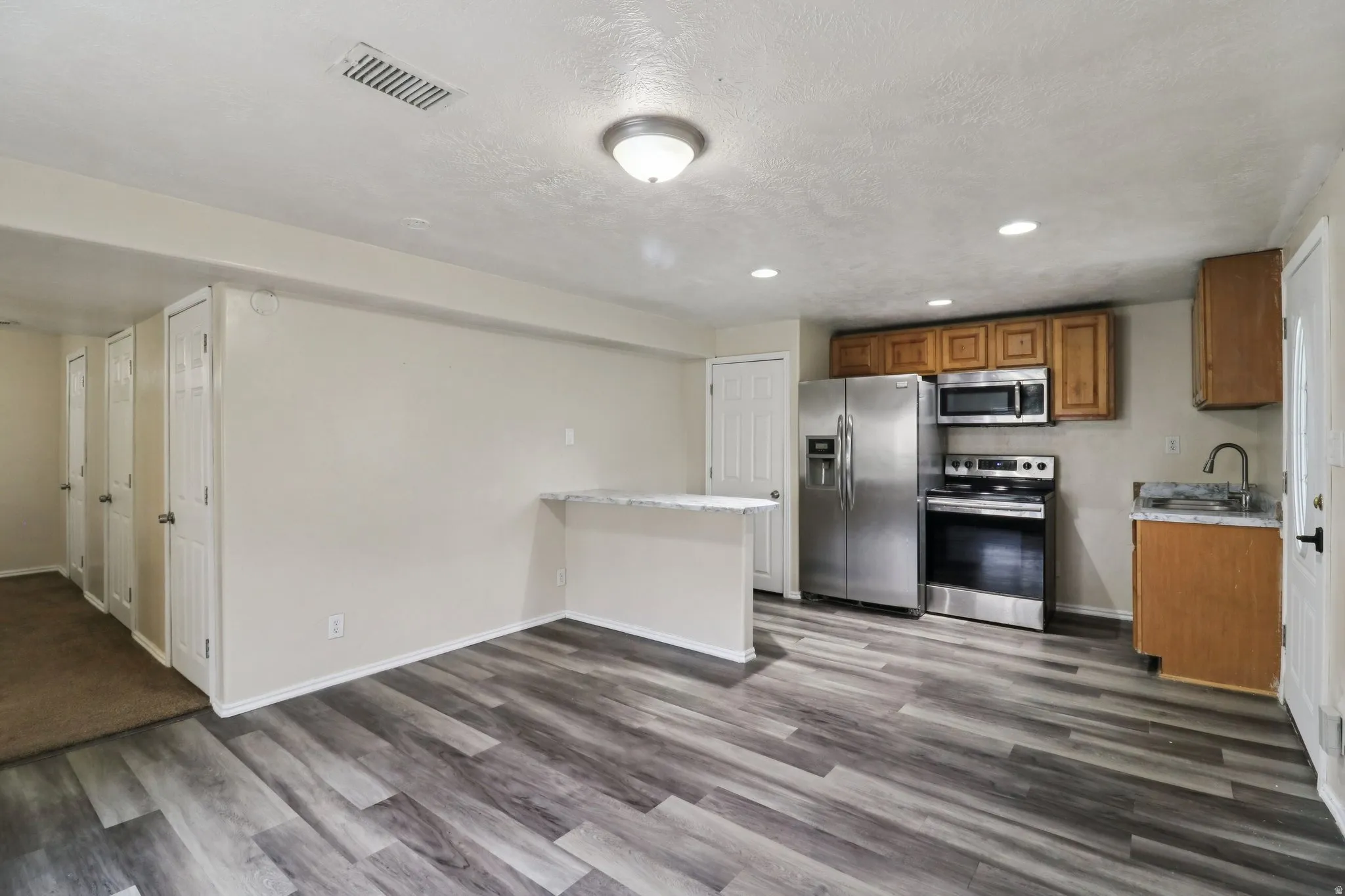 Kitchen with stainless steel appliances, wood finish cabinetry, a peninsula, dark wood-type flooring, and recessed lighting