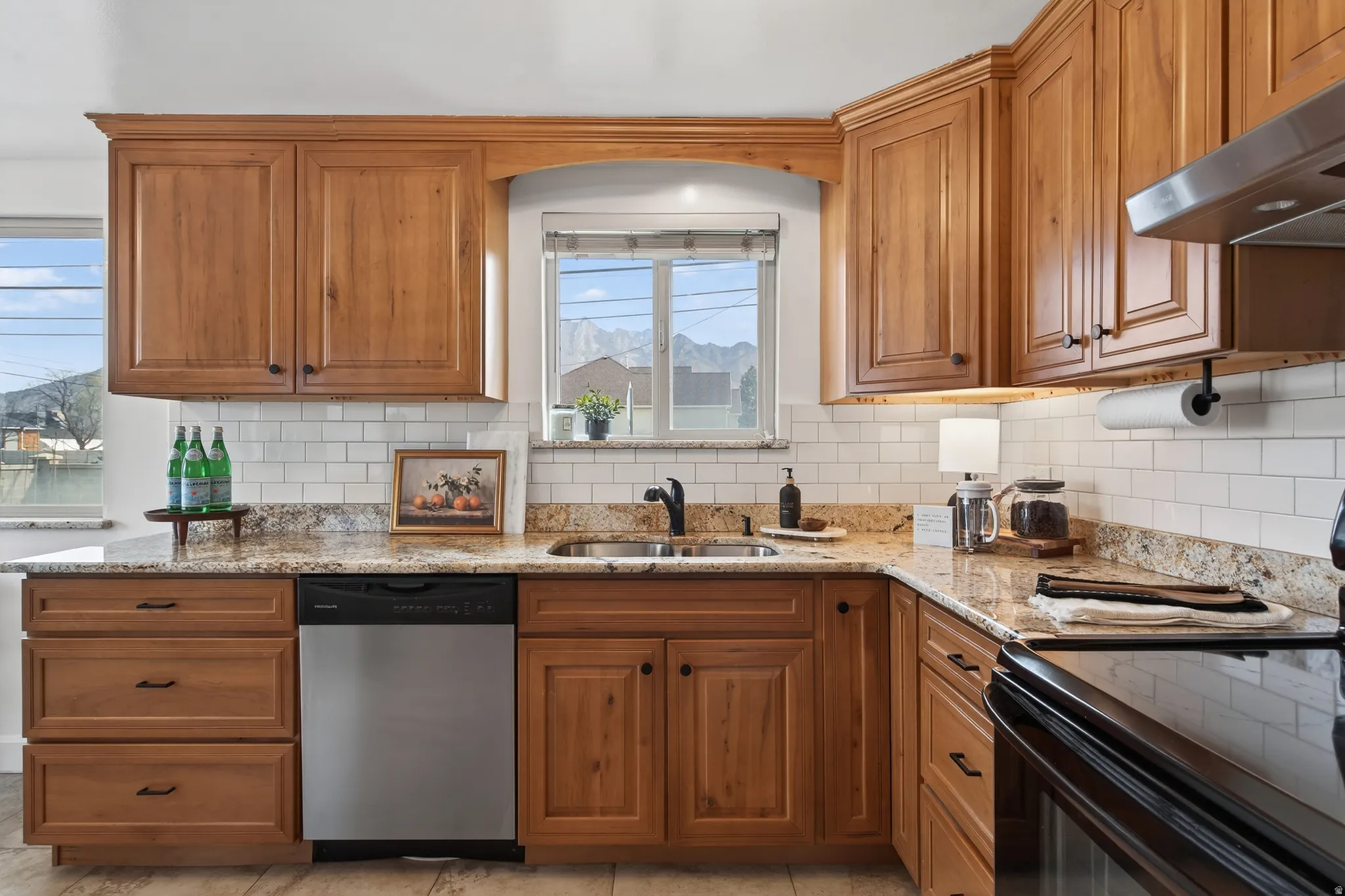 Kitchen featuring black range with electric stovetop, granite counters, dishwasher, wood finish cabinets, and subway tile backsplash