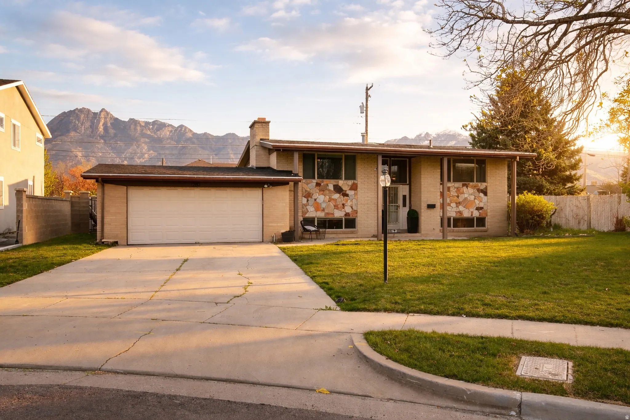 View of front of property featuring brick siding, concrete driveway, a mountain view, and a chimney