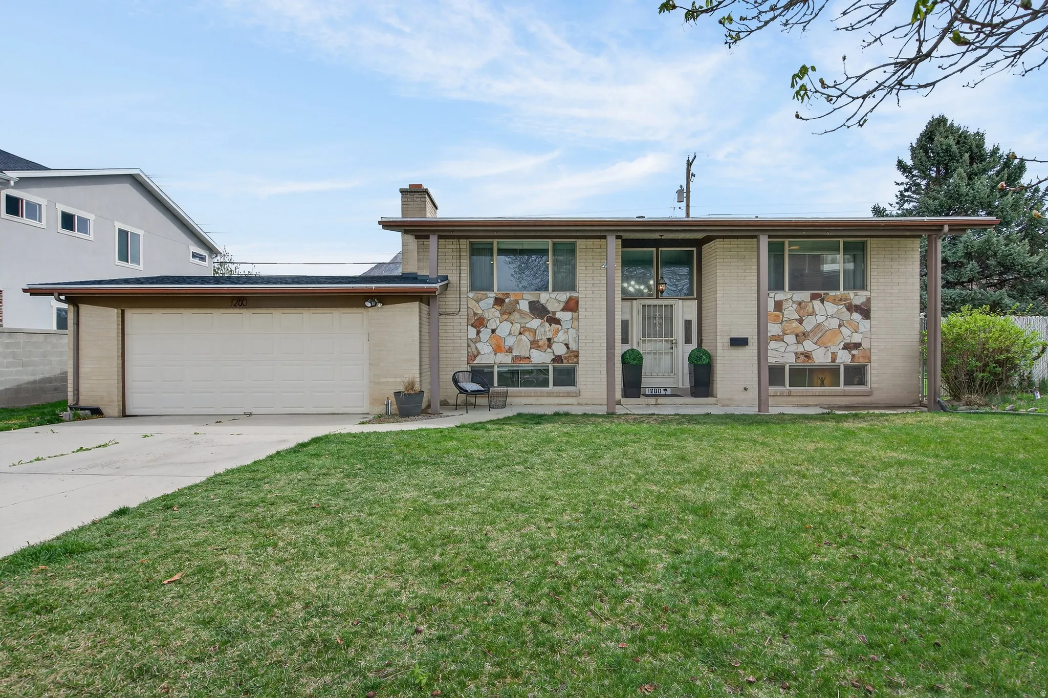 View of front facade featuring brick siding, driveway, a front yard, and a chimney