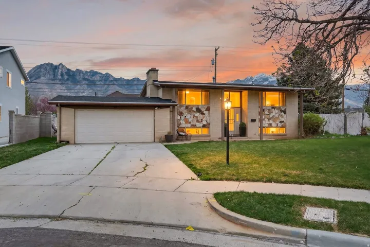 Mid-century modern home with concrete driveway, a chimney, brick siding, an attached garage, and a porch