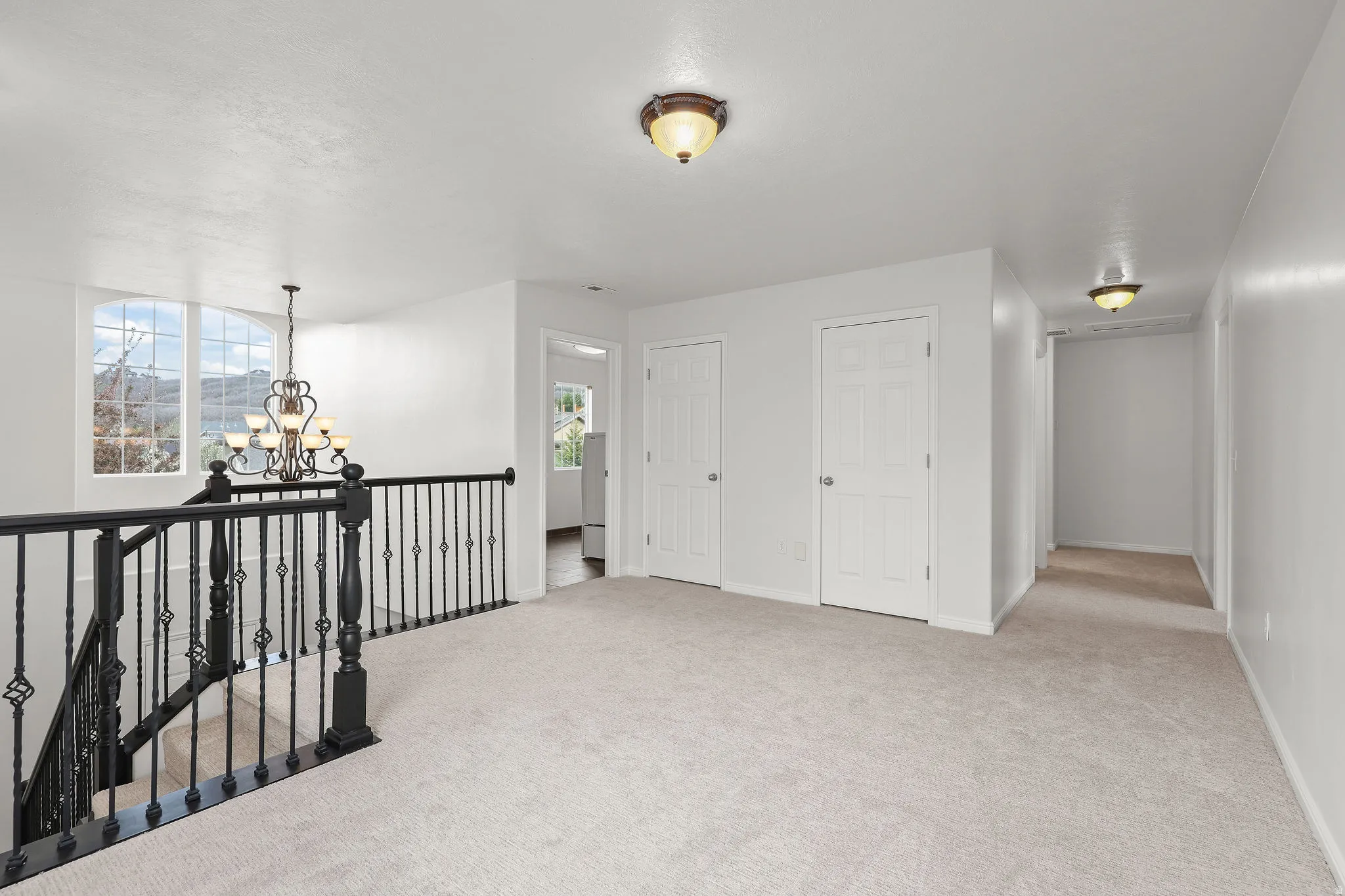 Hall with suspended lighting, light colored carpet, and an upstairs landing