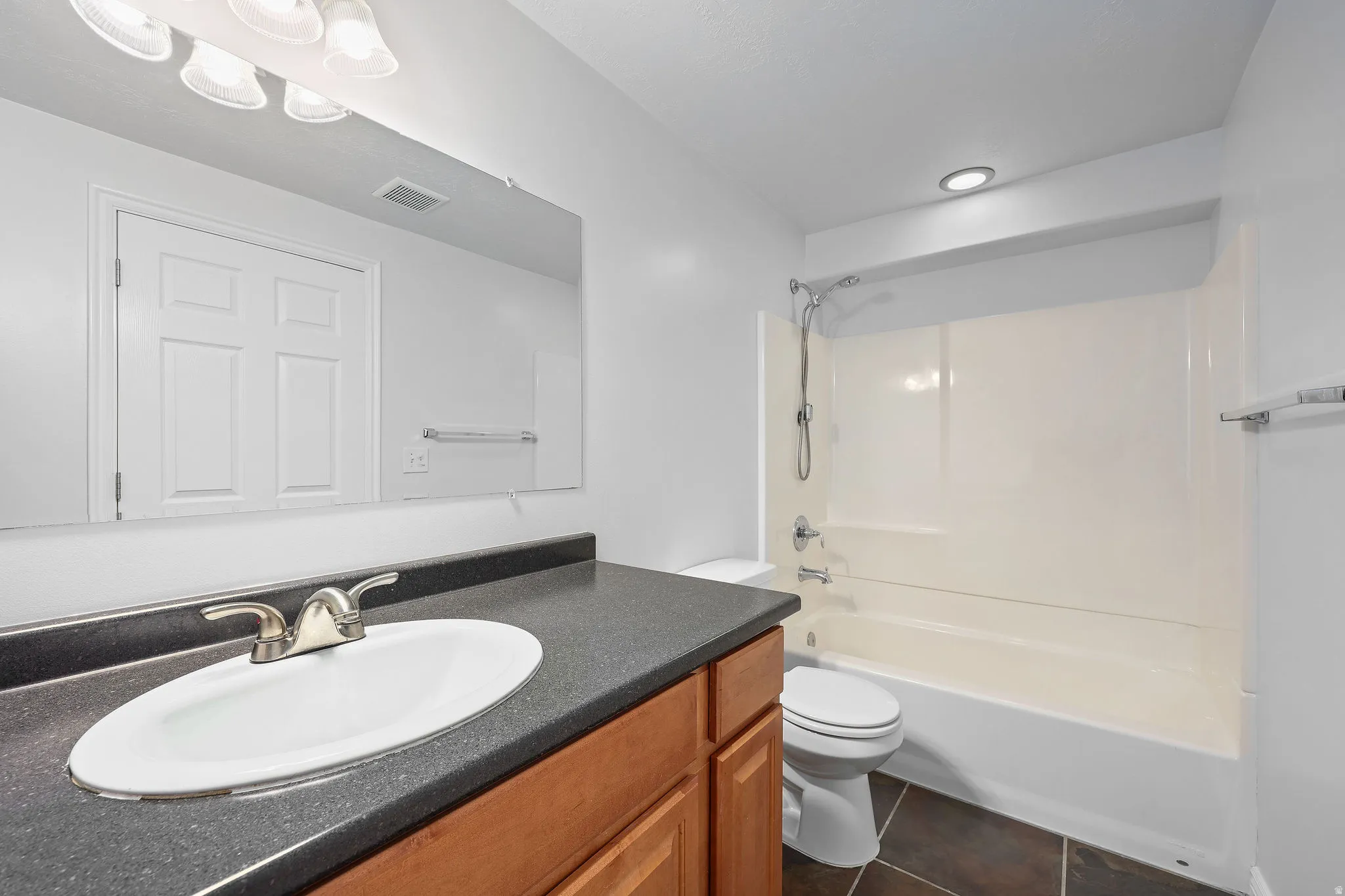 Bathroom with vanity, bathing tub / shower combination, and dark tile patterned flooring