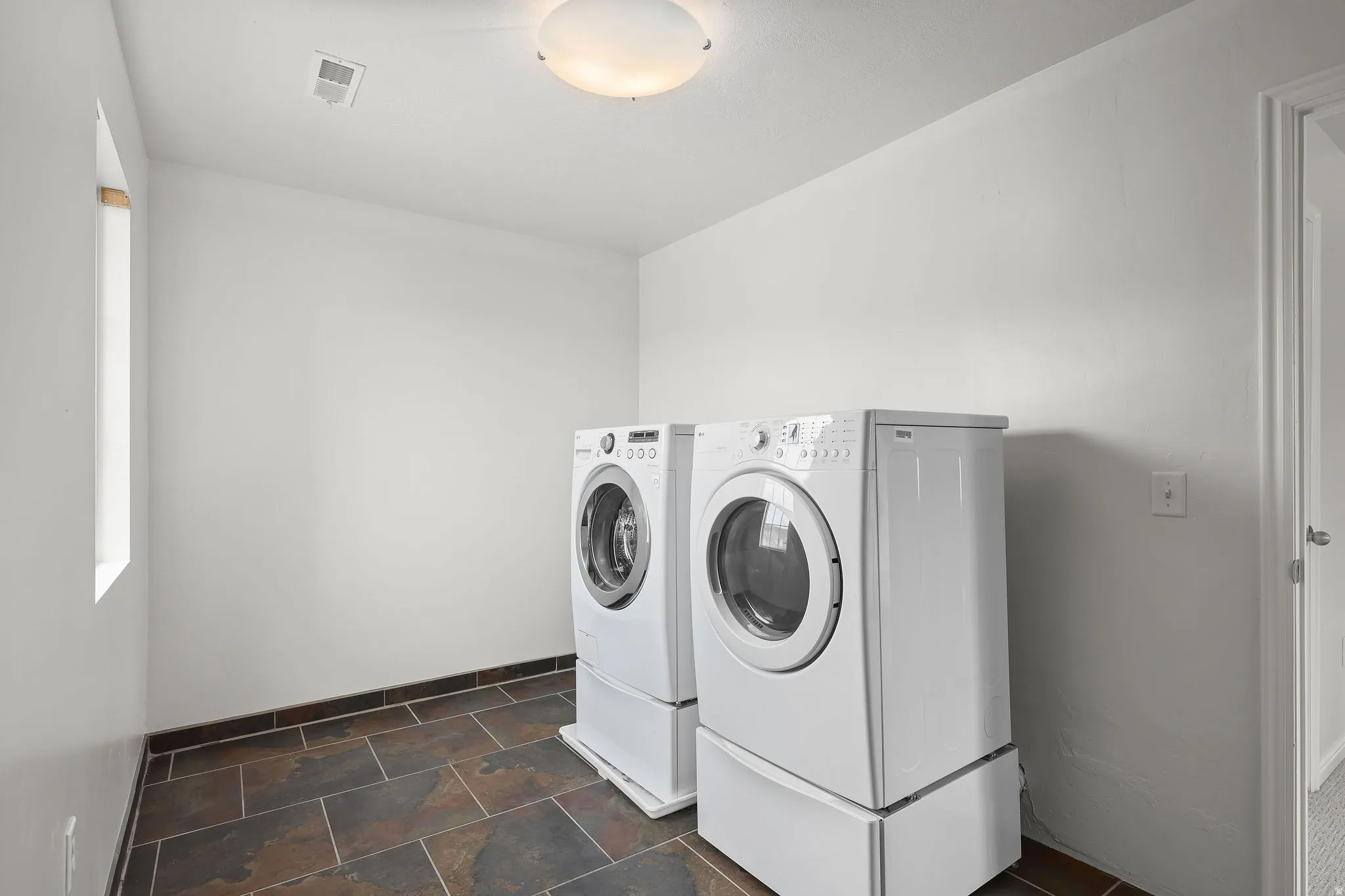 Laundry room with washer and clothes dryer and dark stone finish flooring