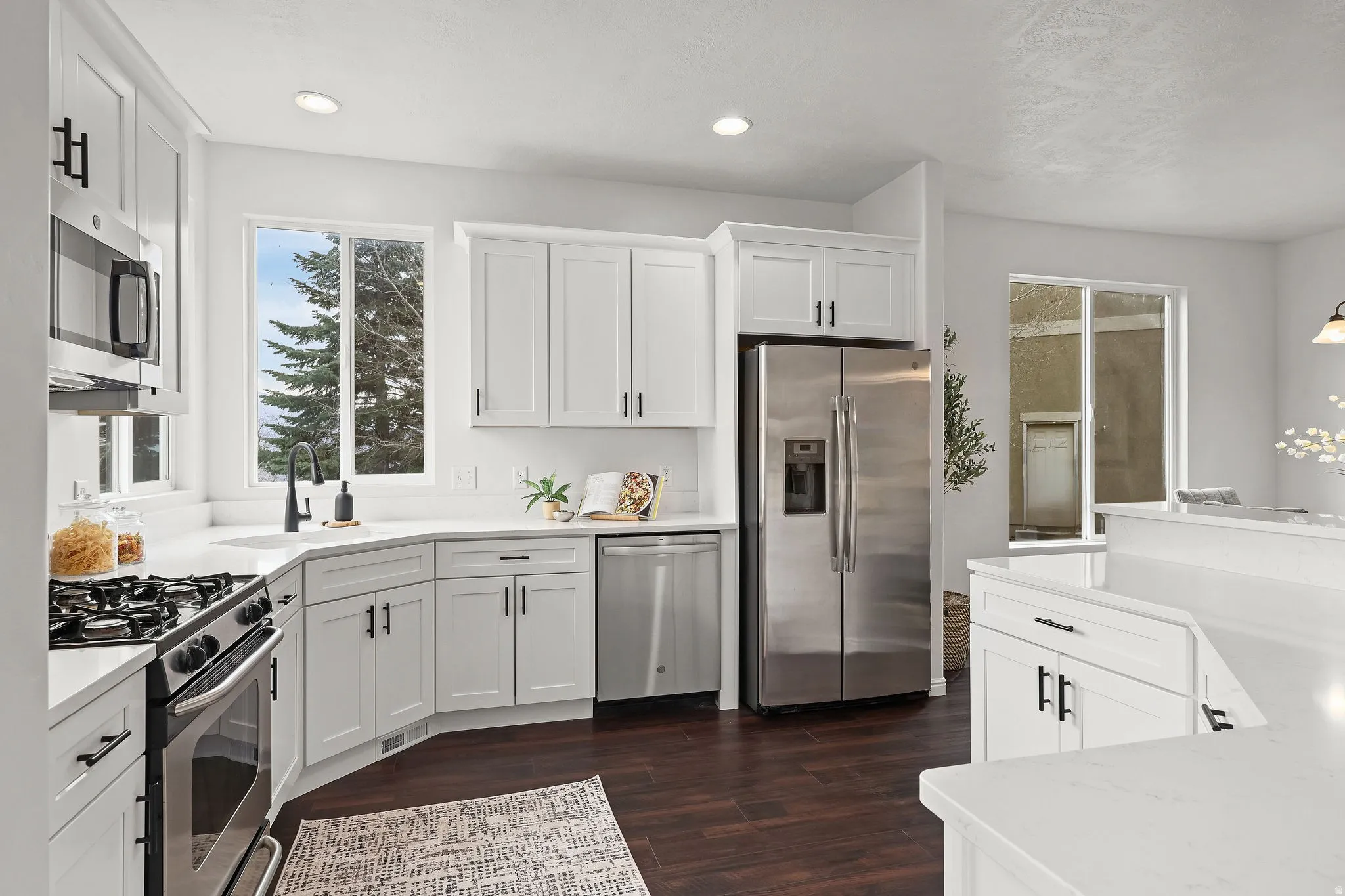 Kitchen with stainless steel appliances, white cabinets, dark wood-style flooring, light stone counters, and recessed lighting