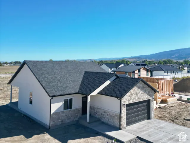 Contemporary exterior with a stone and stucco facade, a dark asphalt shingle roof, an attached garage with a black door, and a concrete driveway