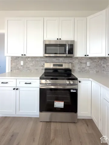 White shaker cabinetry, stone tile backsplash, stainless steel appliances, light-toned wood-finish flooring, and light-toned countertops
