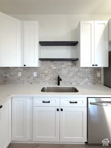 White shaker cabinetry with matte black hardware, stone-finish backsplash, stainless steel sink with matte black faucet, white stone-finish countertop, and stainless steel dishwasher
