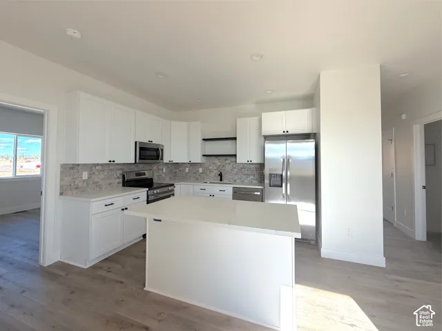 Modern kitchen with white cabinetry and an island, stainless steel appliances, mosaic tile backsplash, and light wood-finish flooring