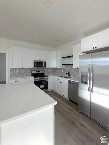White cabinetry with dark hardware, stainless steel appliances, wood-finish flooring, white countertops, and a full backsplash