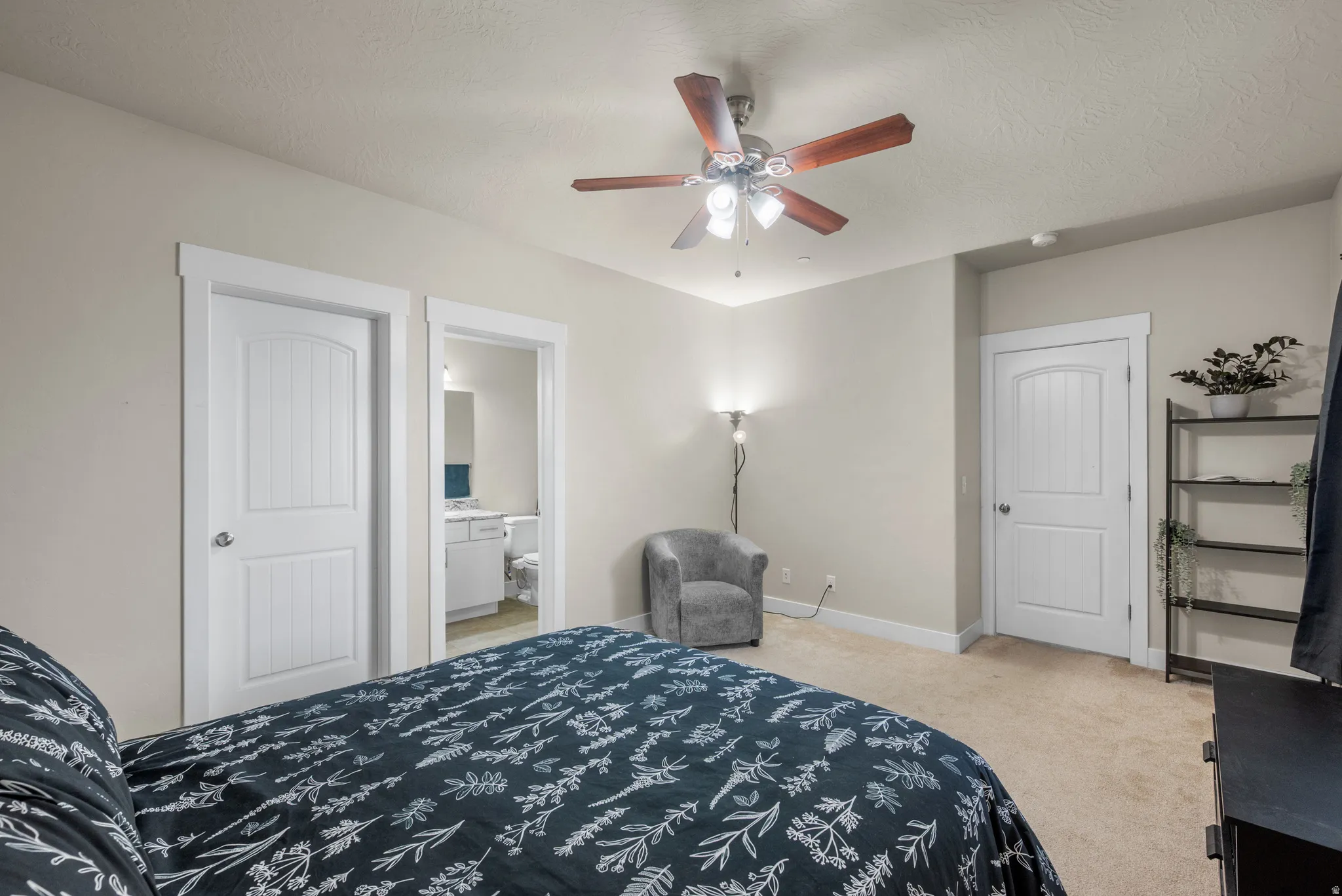 Bedroom featuring light carpet, ensuite bath, ceiling fan, and a textured ceiling