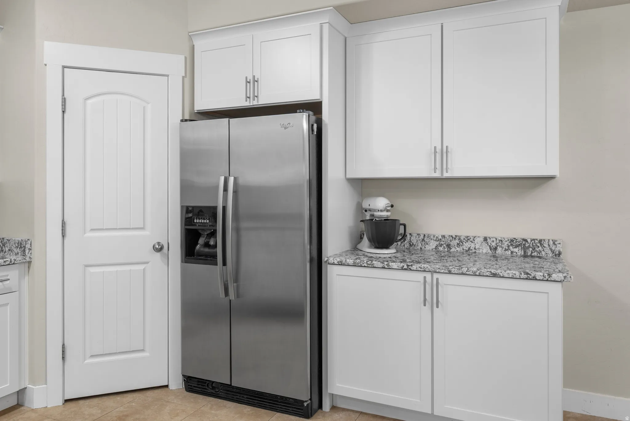 Kitchen with stainless steel fridge with ice dispenser, light stone countertops, white cabinetry, and light tile patterned floors