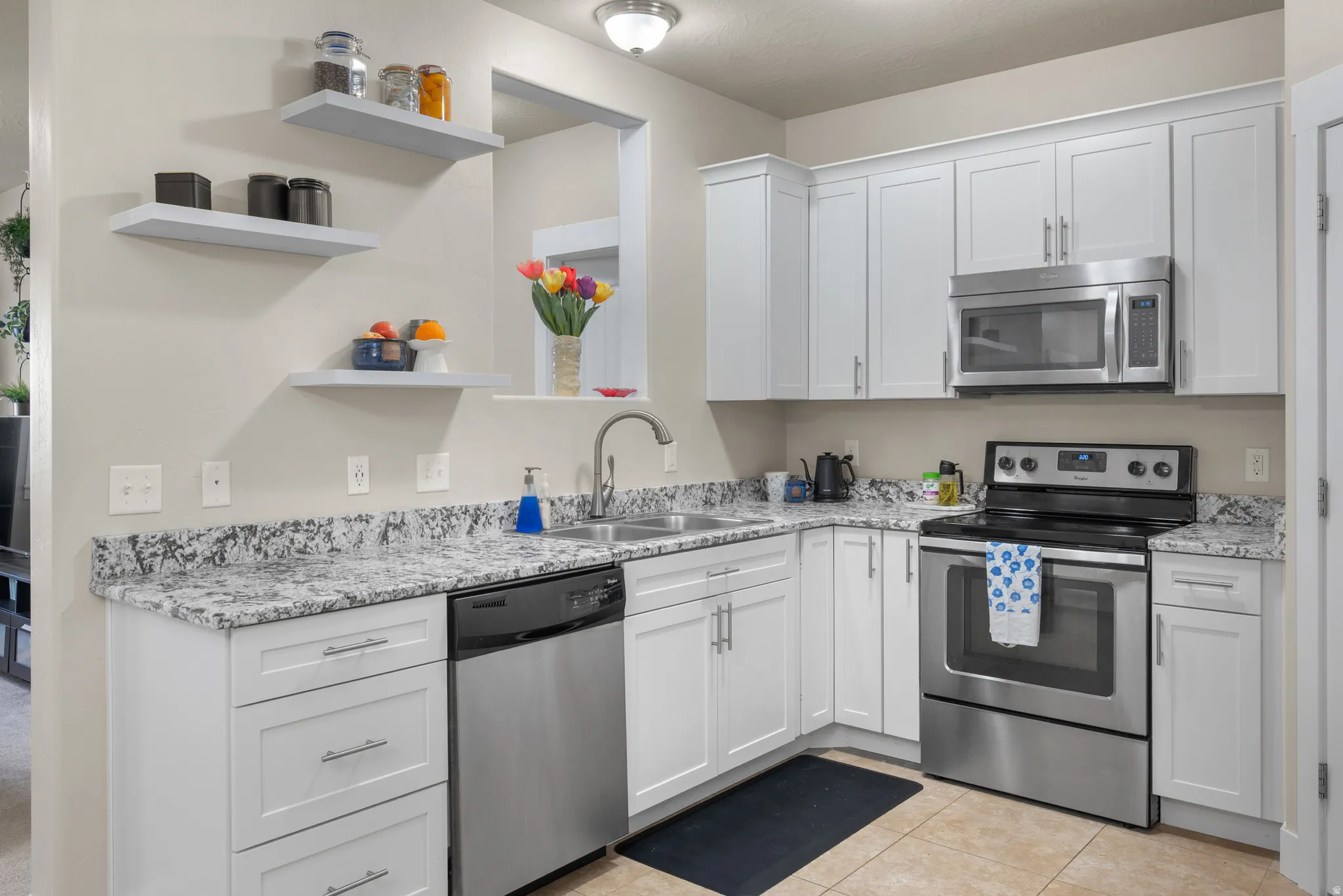 Kitchen featuring stainless steel appliances, white cabinets, open shelves, light tile patterned flooring, and light stone countertops