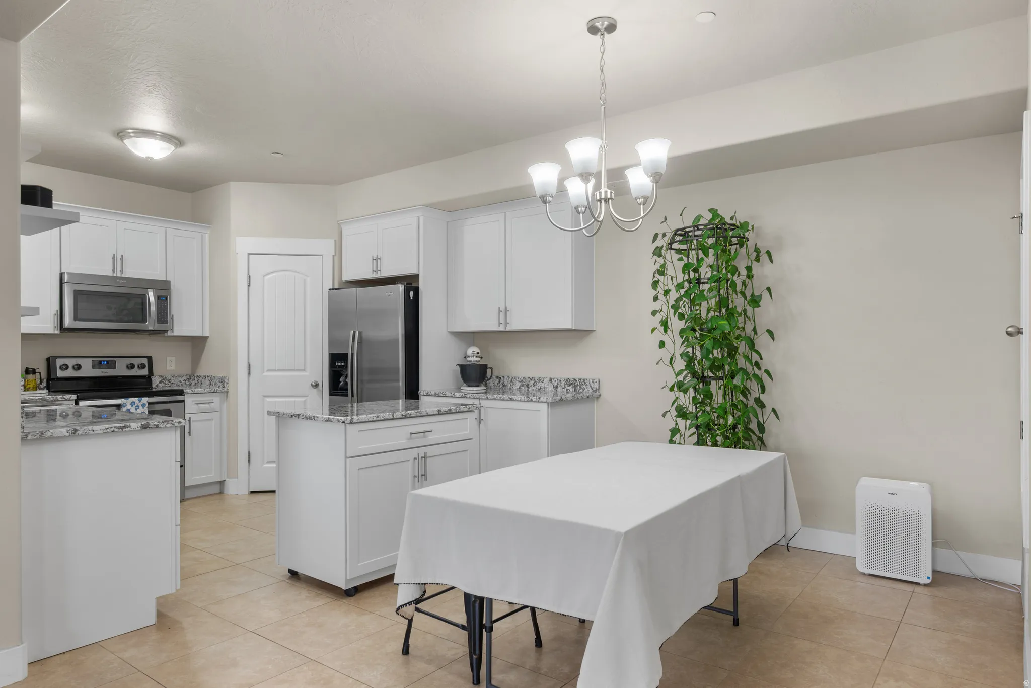 Kitchen with white cabinets, stainless steel appliances, granite stone countertops, a movable center island, and hanging lights