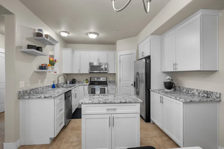 Kitchen with open shelves, stainless steel appliances, white cabinets, a movable kitchen island, and granite stone counters