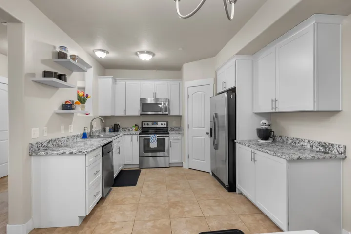 Kitchen with open shelves, stainless steel appliances, white cabinetry, light tile patterned floors, and granite stone counters