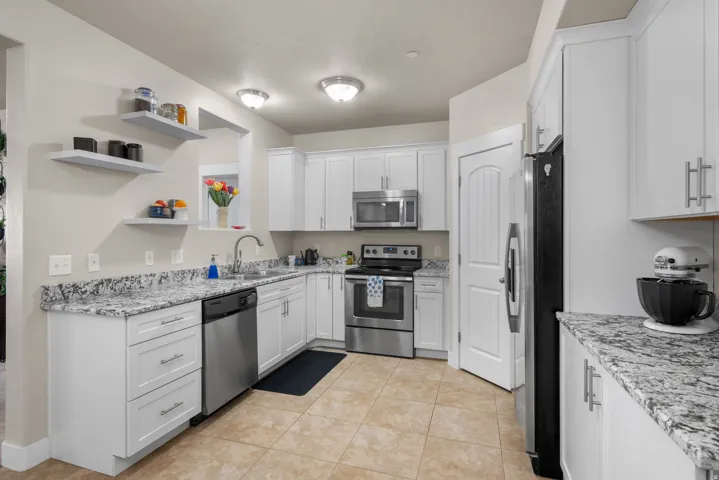 Kitchen featuring stainless steel appliances, white cabinets, open shelves, and granite stone countertops