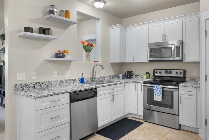 Kitchen featuring stainless steel appliances, white cabinets, open shelves, light tile patterned flooring, and light stone countertops