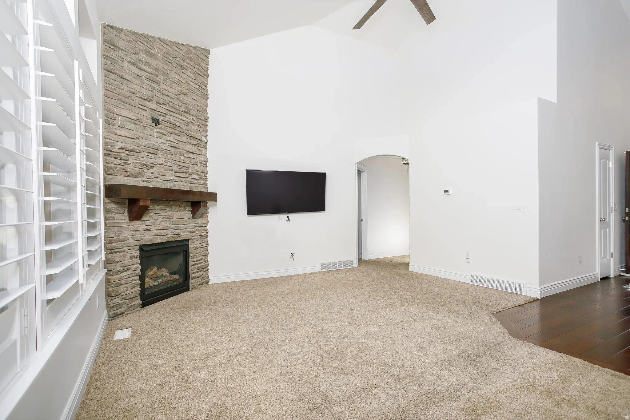 Unfurnished living room featuring a fireplace, arched walkways, ceiling fan, carpet floors, and vaulted ceiling