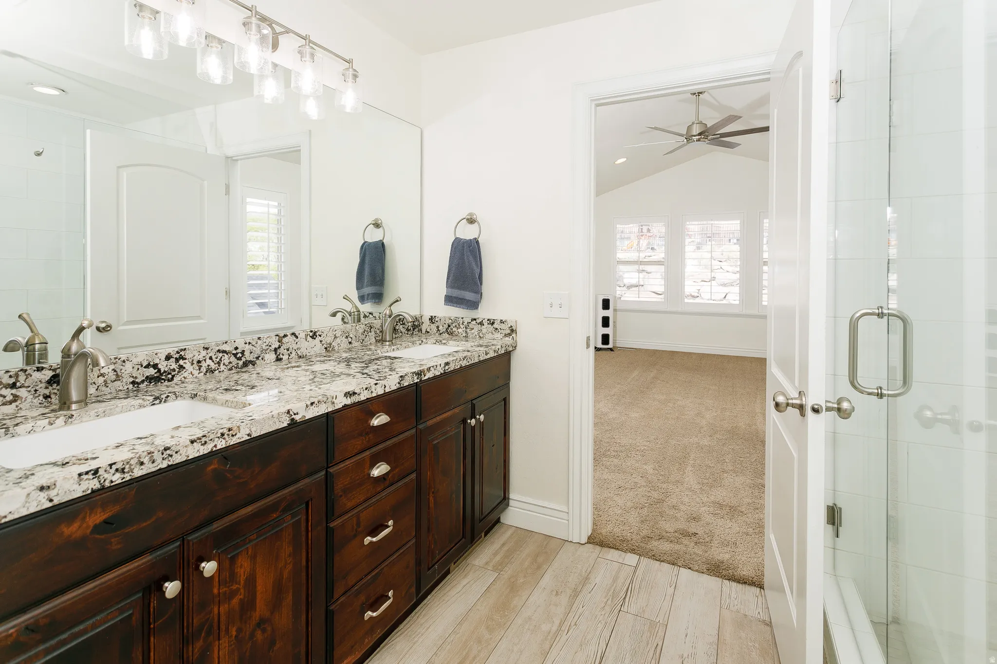 Bathroom with double vanity, a shower stall, plenty of natural light, light wood-style flooring, and lofted ceiling