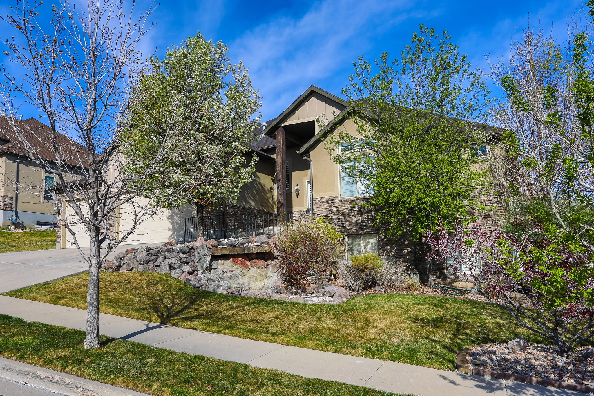 View of property hidden behind natural elements with a front yard, stone siding, stucco siding, and driveway