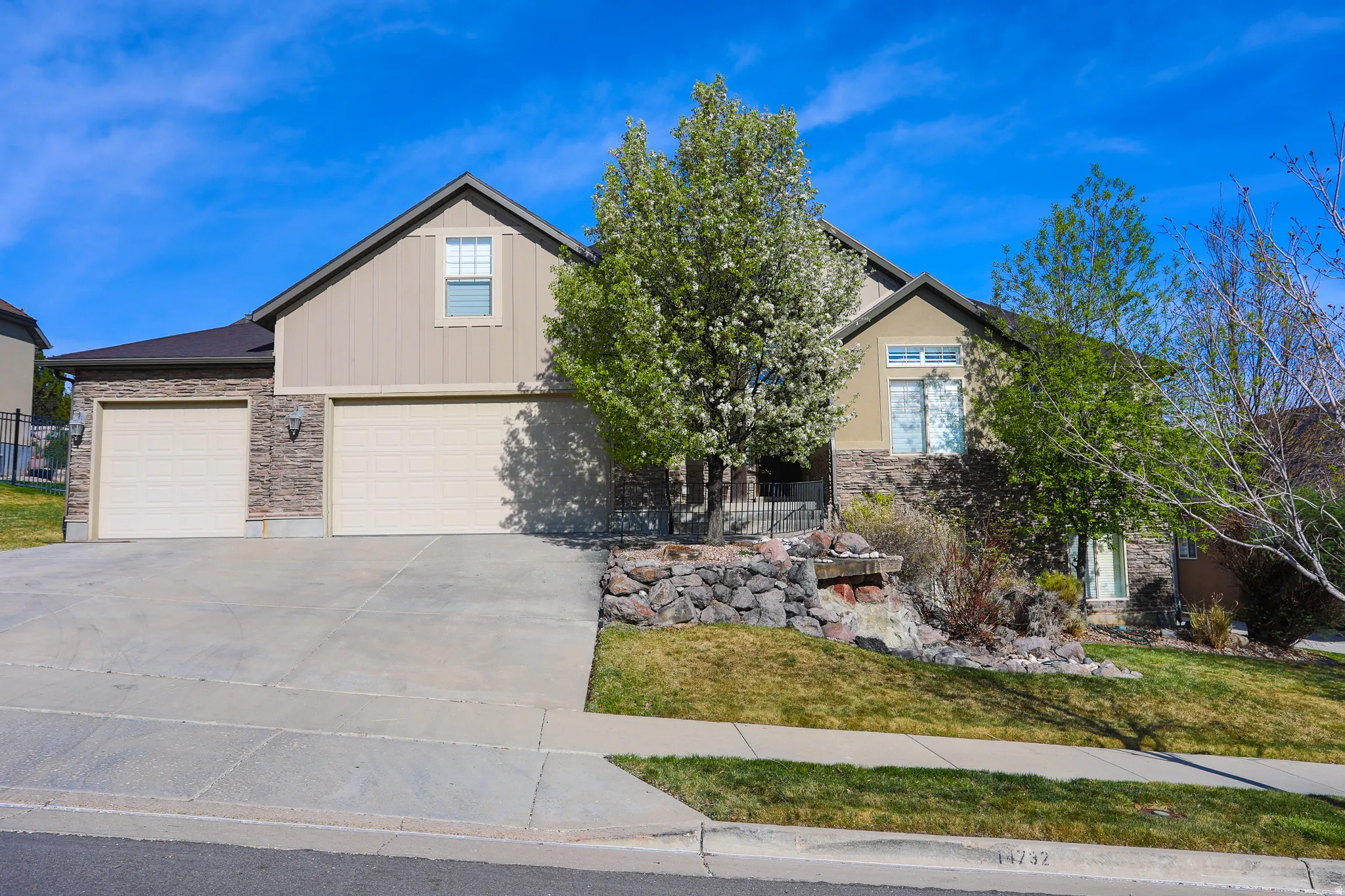 View of front of house featuring concrete driveway, stone siding, a front yard, a garage, and board and batten siding