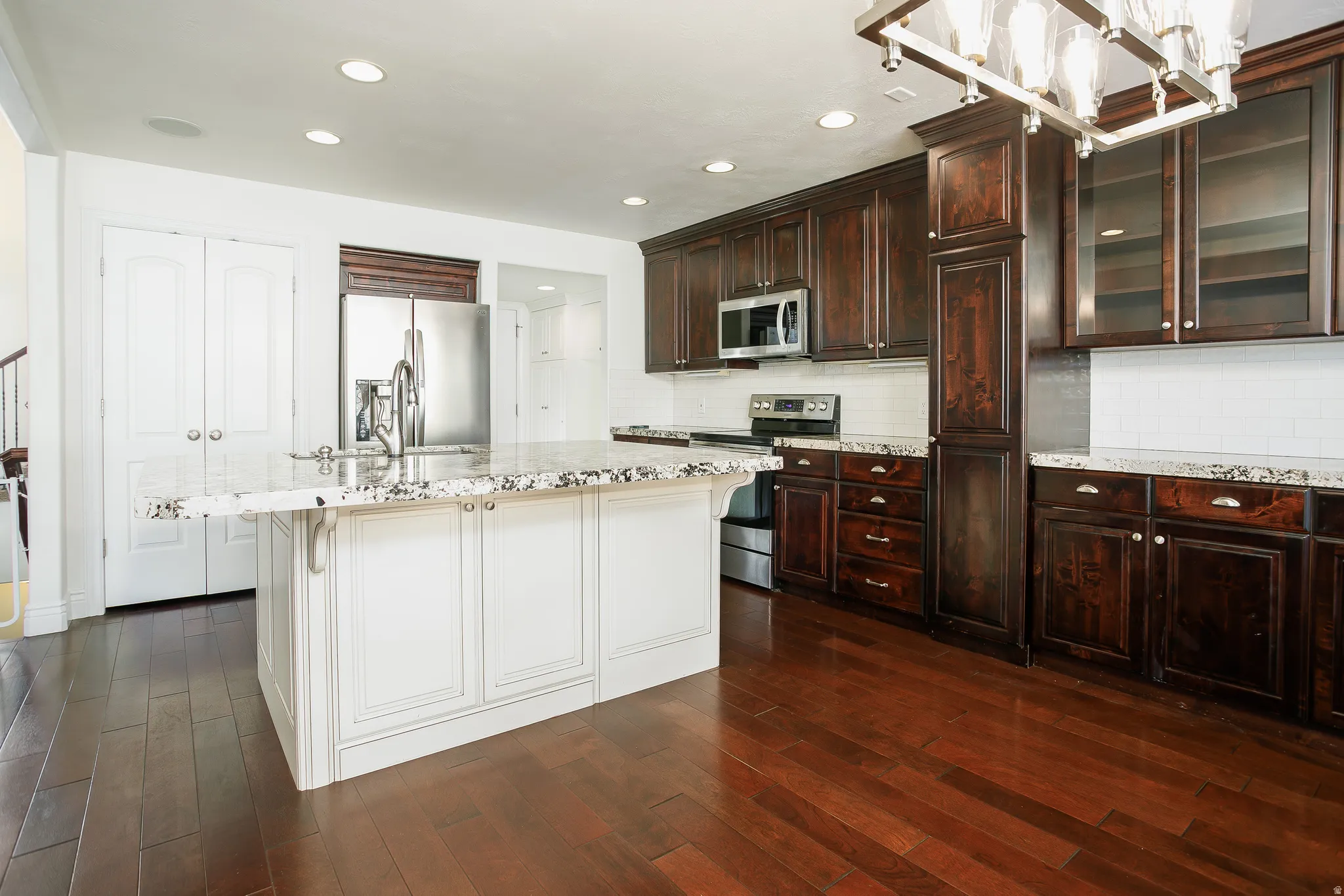 Kitchen with light stone countertops, stainless steel appliances, dark wood-style flooring, an island with sink, and two tone cabinets
