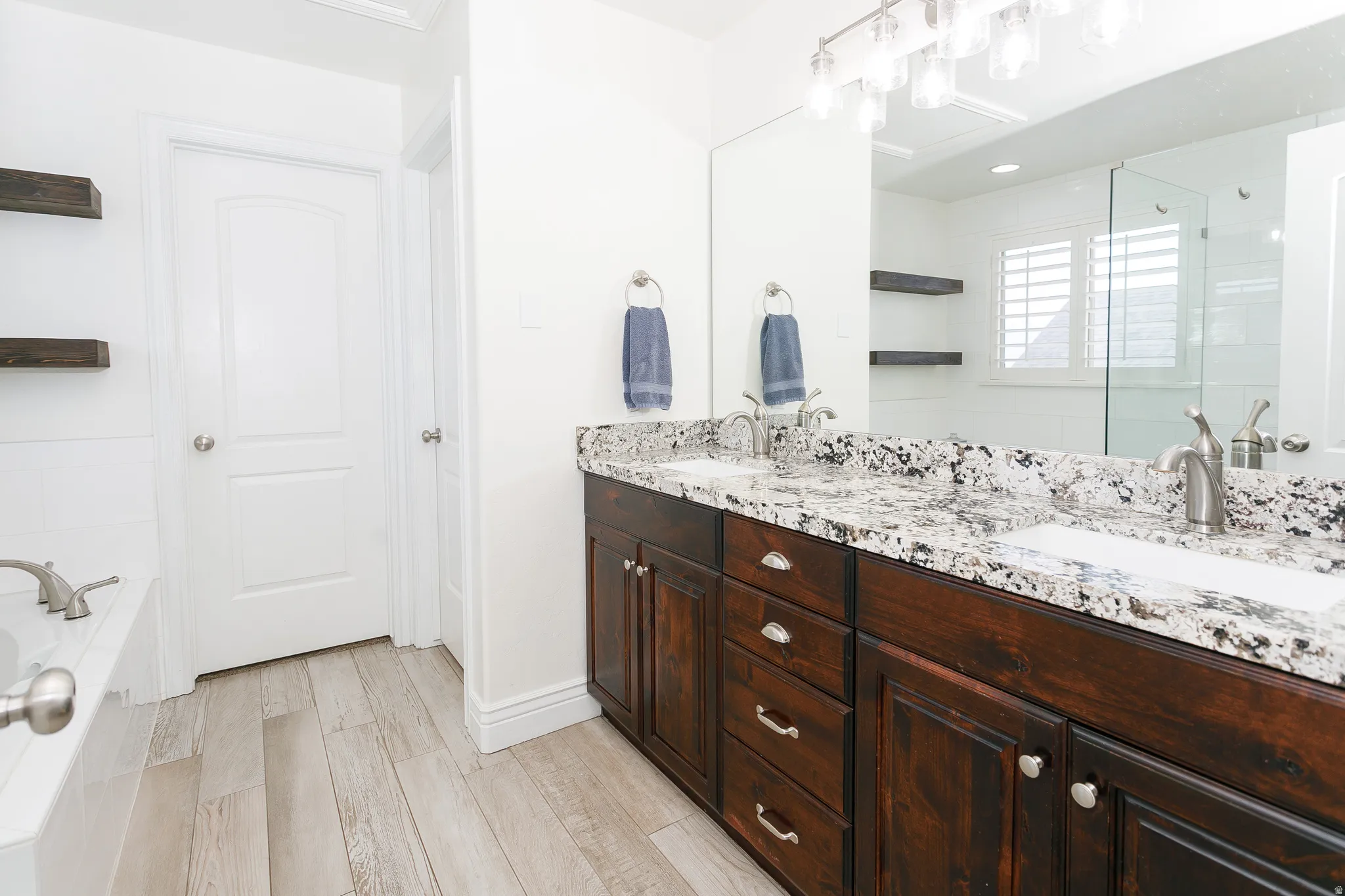 Bathroom featuring double vanity, light wood-style flooring, a garden tub, and a stall shower