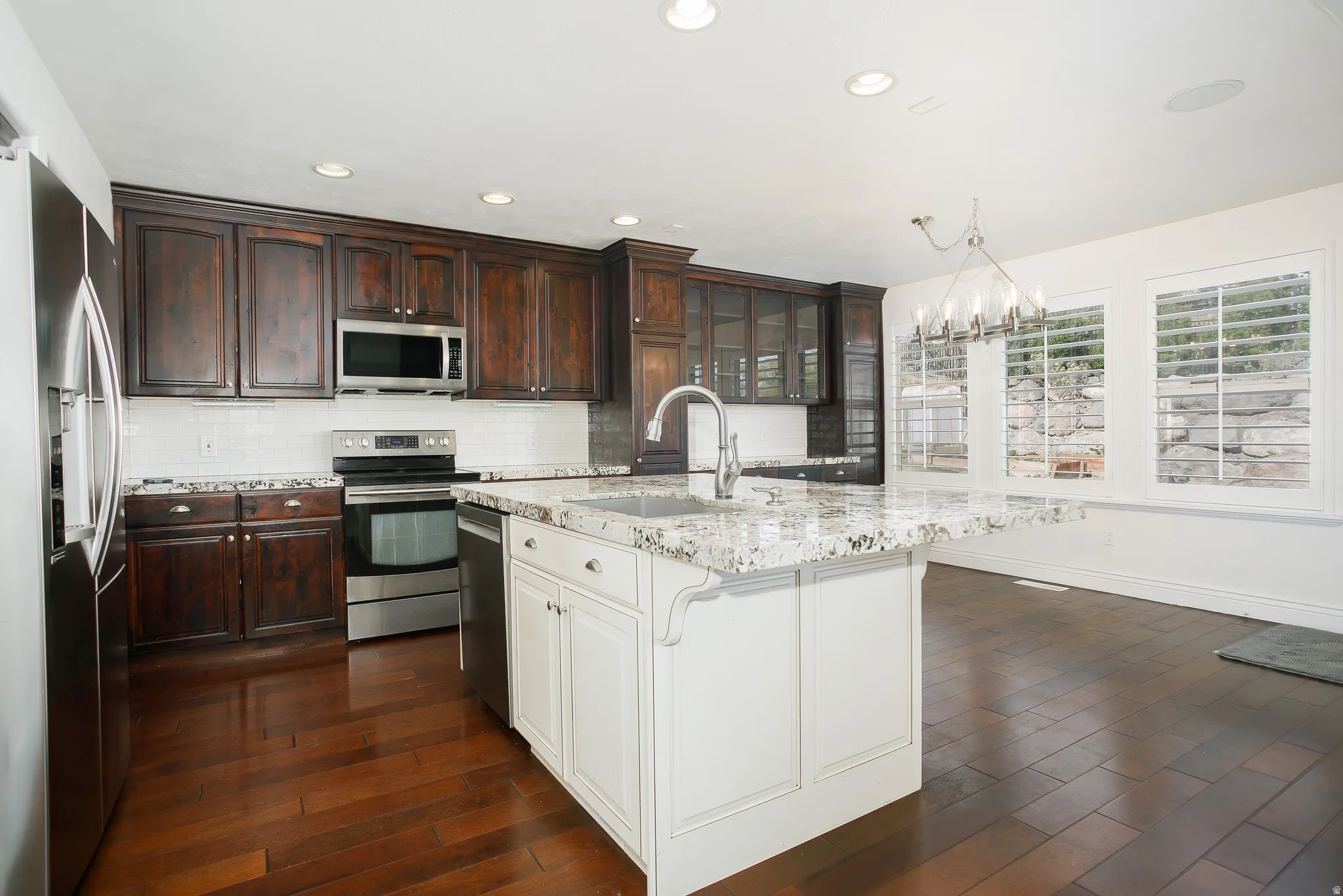 Kitchen featuring stainless steel appliances, light stone countertops, a chandelier, two tone cabinets, and dark wood-style floors