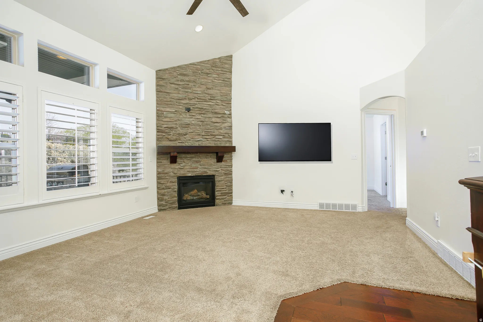 Unfurnished living room featuring a stone fireplace, arched walkways, carpet flooring, ceiling fan, and lofted ceiling
