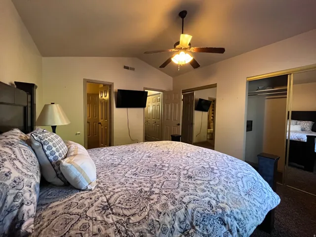 Bedroom featuring lofted ceiling, a ceiling fan, two closets, and dark carpet