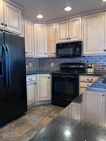 Kitchen with black appliances, recessed lighting, backsplash, dark stone counters, and stone tile flooring