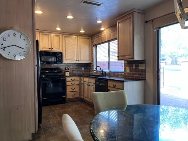 Kitchen featuring dark countertops, black appliances, tasteful backsplash, stone finish floors, and recessed lighting