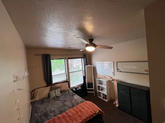 Bedroom with a ceiling fan, a textured ceiling, and dark carpet