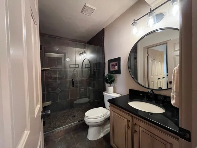Full bathroom featuring vanity, a stall shower, and dark tile patterned floors