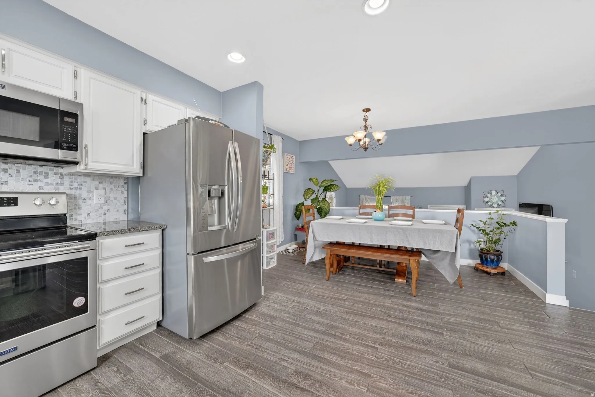 Kitchen featuring stainless steel appliances, white cabinets, a chandelier, light wood finished floors, and vaulted ceiling