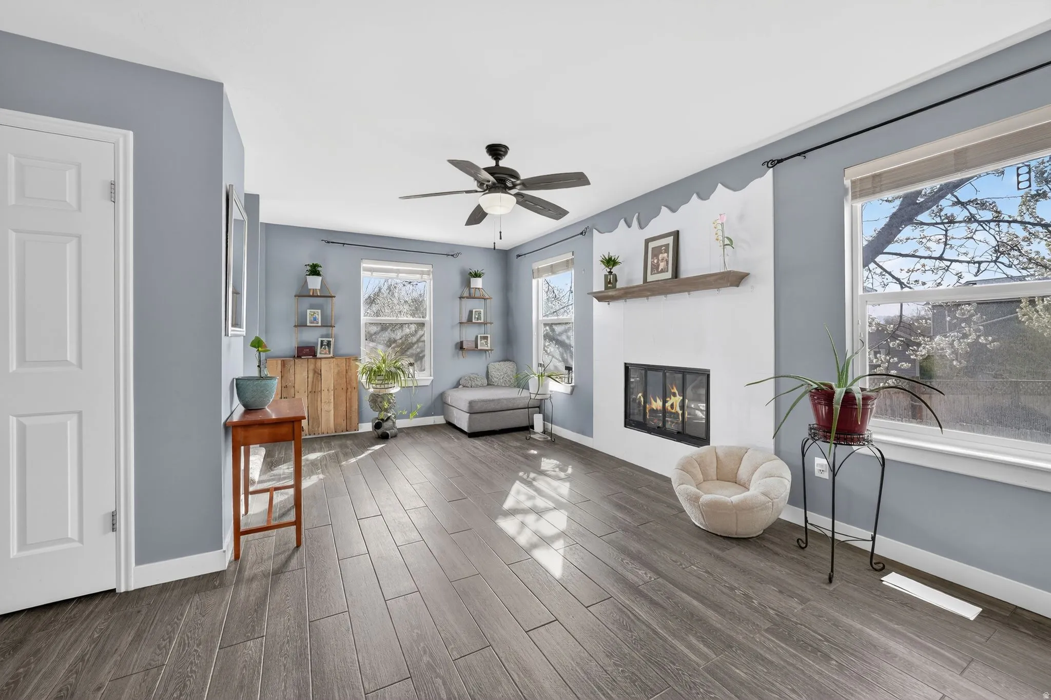 Living area with wood finished floors, a glass covered fireplace, and a ceiling fan
