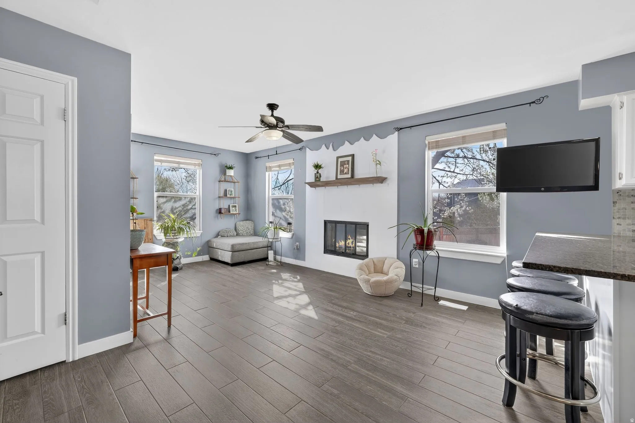 Living room featuring healthy amount of natural light, dark wood-style floors, a glass covered fireplace, and ceiling fan
