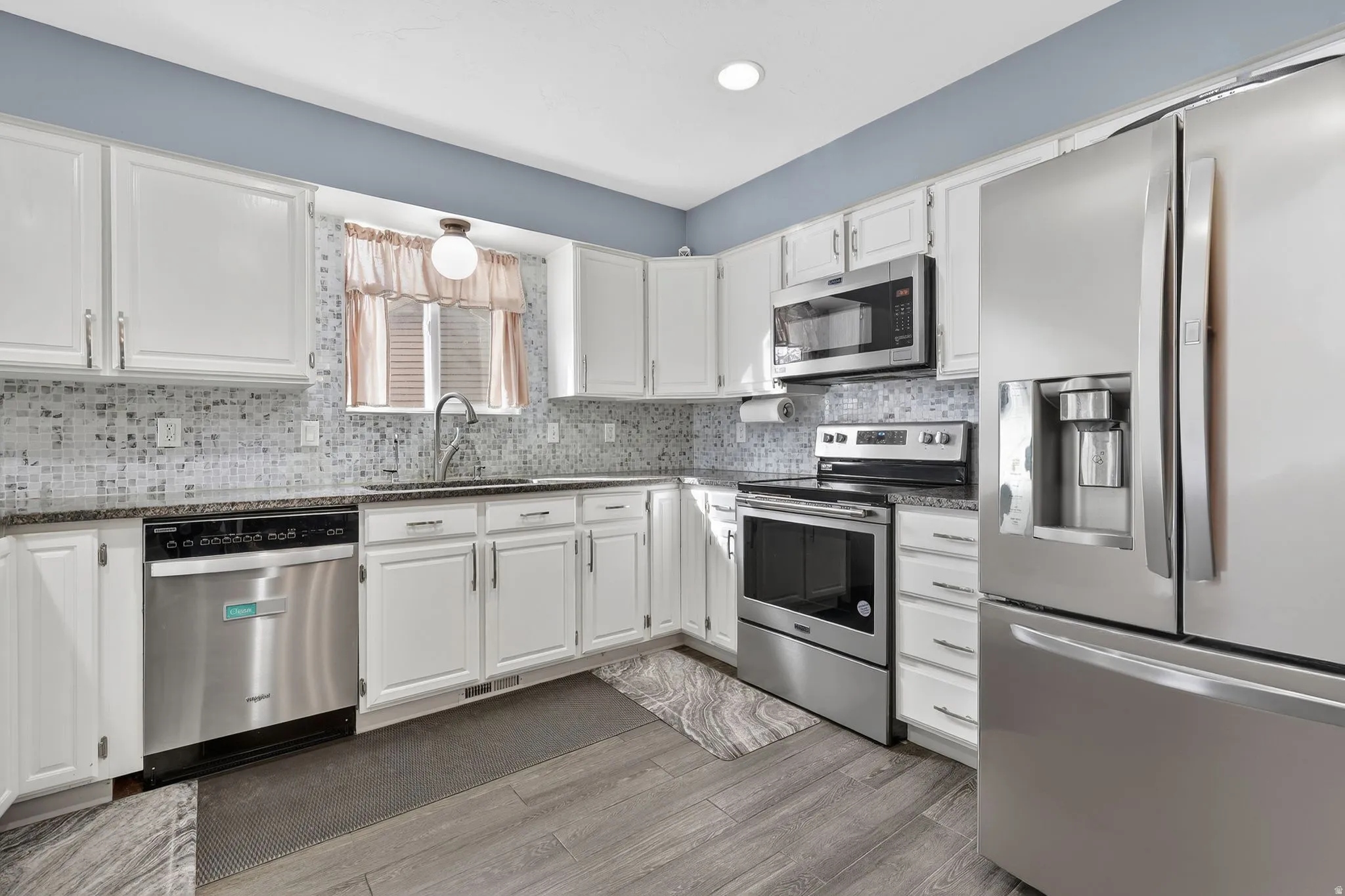 Kitchen featuring stainless steel appliances, white cabinetry, light wood-style floors, dark stone counters, and recessed lighting