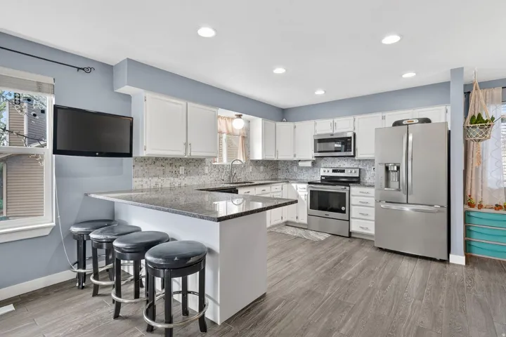 Kitchen featuring stainless steel appliances, a peninsula, a kitchen bar, tasteful backsplash, and recessed lighting