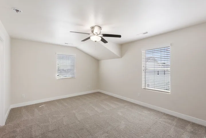 Unfurnished room featuring vaulted ceiling, ceiling fan, and light carpet