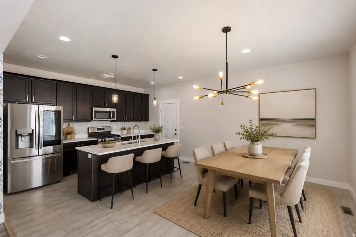 Open-concept kitchen and dining area featuring dark wood cabinetry, stainless steel appliances, a center island with countertop seating, and light wood-finish flooring