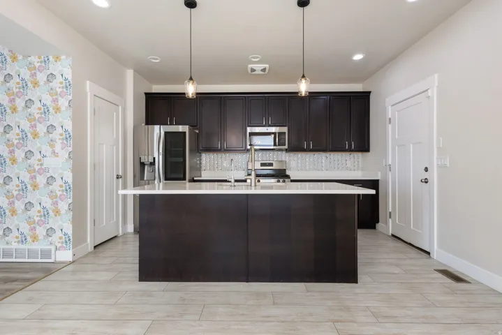 Kitchen with wood finish floors, decorative light fixtures, an island with sink, stainless steel appliances, and backsplash