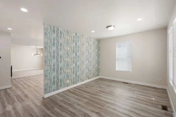 Unfurnished room featuring an accent wall, light wood-style floors, suspended lighting, and wallpapered walls