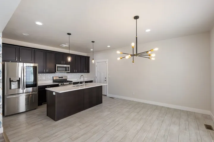 Kitchen featuring stainless steel appliances, a center island with sink, backsplash, suspended lighting, and light wood-type flooring