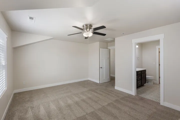 Unfurnished bedroom with light carpet, a ceiling fan, and connected bathroom