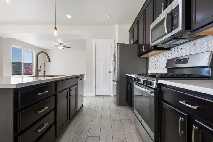 Kitchen featuring stainless steel appliances, tasteful backsplash, a center island with sink, dark cabinetry, and light stone countertops