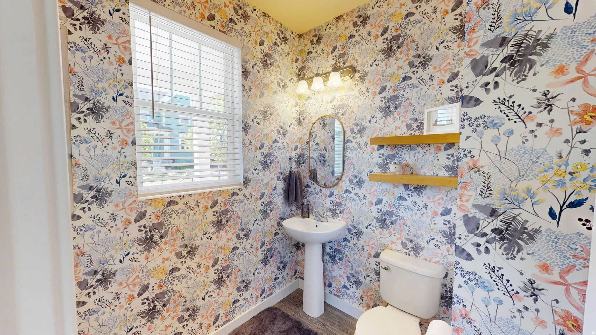 Half bathroom featuring wallpapered walls and wood finished floors