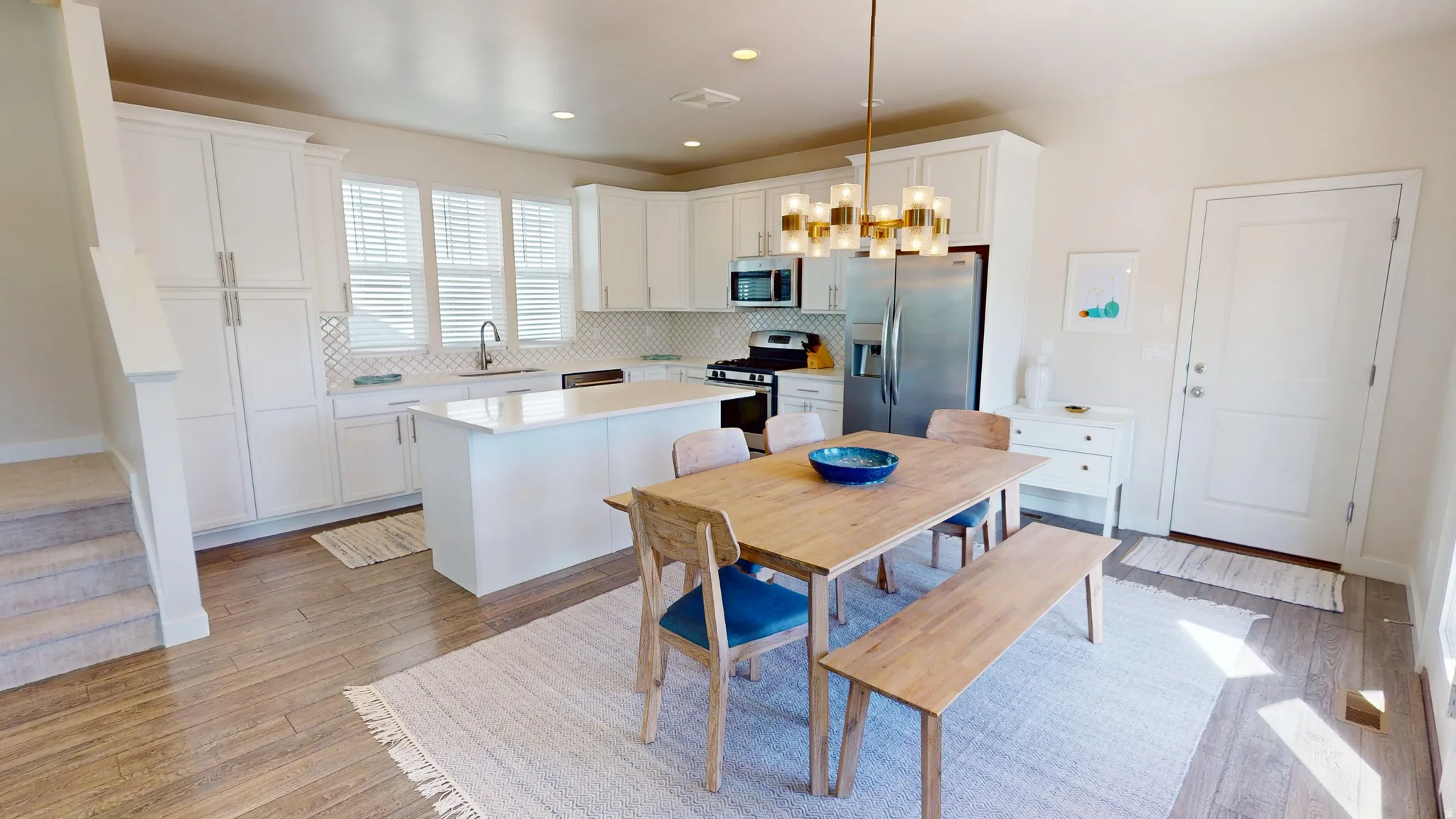 Kitchen with white cabinets, stainless steel appliances, light wood finished floors, a kitchen island, and tasteful backsplash